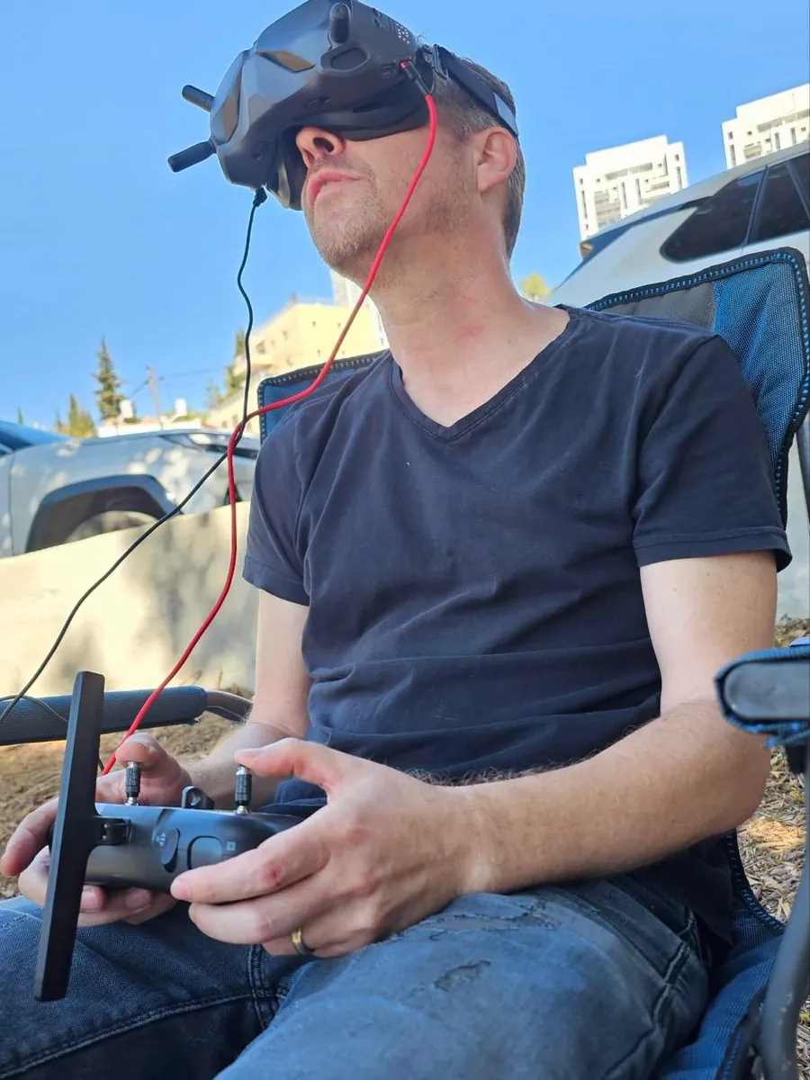 גילי חן יושב עם משקפי טיסה על העיניים ומחזיק שלט רחפן, במהלך טיסת FPV